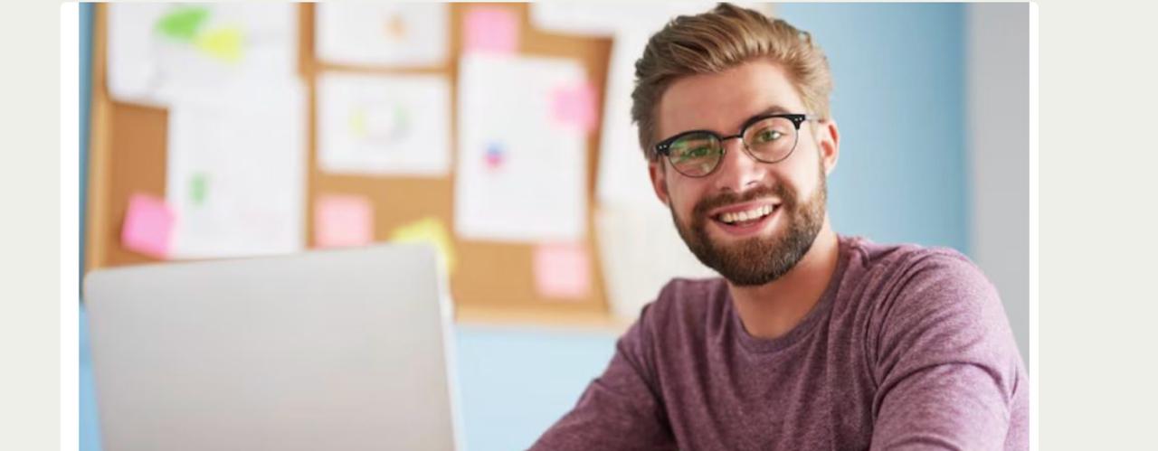 Lächelnder Mann sitzt an einem Schreibtisch und arbeitet an seinem Laptop
